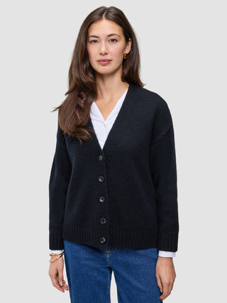 Eine Frau trägt eine schwarze, grob gestrickte, weiche Wollstrickjacke für Damen über einem weißen Hemd und einer blauen Jeans.