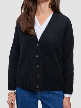 Eine Person, die eine schwarze, grob gestrickte, weiche Wollstrickjacke für Damen über einem weißen Hemd mit Kragen und einer blauen Jeans trägt.