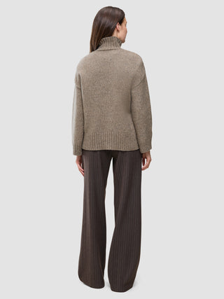 Eine Person, von hinten gesehen, die einen taupefarbenen, melierten Damen-Rollkragenpullover aus dicker, weicher Wolle und eine dunkle Nadelstreifenhose trägt.