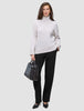 Eine Frau, die einen beigen Rollkragenpullover und eine schwarze Women GO2 Pants Straight trägt und eine schwarze Handtasche in der Hand hält.