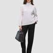 Eine Frau, die einen beigen Rollkragenpullover und eine schwarze Women GO2 Pants Straight trägt und eine schwarze Handtasche in der Hand hält.