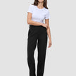 Eine Frau in einem weißen T-Shirt mit Rundhalsausschnitt, einer schwarzen Women GO2-Hose in gerader Passform und dunkelbraunen Loafern, die ein minimalistisches skandinavisches Design widerspiegeln.