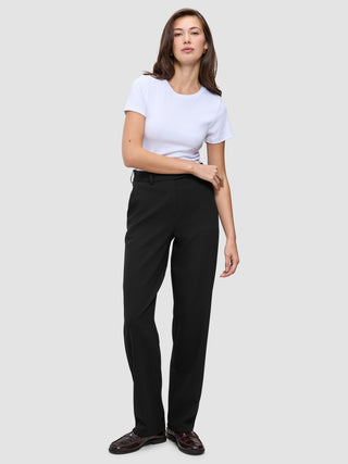 Eine Frau in einem weißen T-Shirt mit Rundhalsausschnitt, einer schwarzen Women GO2-Hose in gerader Passform und dunkelbraunen Loafern, die ein minimalistisches skandinavisches Design widerspiegeln.
