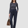 Eine Frau in einem dunkelgrauen Langarmhemd aus Doubleface-Stoff und einer Women GO2 Pants Straight Blue Nights, die eine braune Wildleder-Tragetasche bei sich trägt.