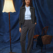 Eine Frau in einer dunkelgrauen Jacke aus Doubleface-Stoff und einem hellblauen Hemd mit Knöpfen, die eine Women GO2 Pants Straight Dark Grey Melange trägt und vor einem blauen Hintergrund steht.