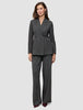 Eine Frau, die einen Women Nara Blazer Fitted Black Check in anthrazitgrauem Karomuster trägt, dazu eine passende Hose mit weitem Bein.