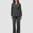Eine Frau, die einen Women Nara Blazer Fitted Black Check in anthrazitgrauem Karomuster trägt, dazu eine passende Hose mit weitem Bein.