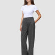 Eine Frau, die ein schlichtes weißes T-Shirt und die Women Nara Pants Wide Black Check trägt, die schwarz sind und ein dezentes graues Karomuster aufweisen.