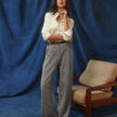 Eine Frau, die ein weißes Women’s Oxford Shirt White Orchid Slim und eine graue Hose trägt, steht vor einem blauen Stoffhintergrund.