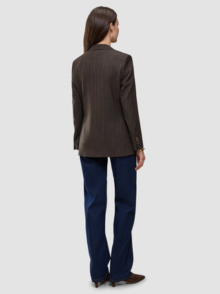 Eine Person, von hinten gesehen, die einen Women Serene Blazer Regular Walnut Herringbone, eine dunkelblaue Jeans und braune Schuhe trägt.
