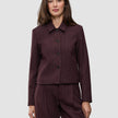 Eine Frau trägt die Women Serene Short Jacket Berry Pinstripe – eine Jacke aus dunkelviolettem Stoff mit Nadelstreifen, die sich durch eine kastenförmige Passform und eine kurze Silhouette auszeichnet.