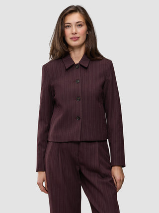 Eine Frau trägt die Women Serene Short Jacket Berry Pinstripe – eine Jacke aus dunkelviolettem Stoff mit Nadelstreifen, die sich durch eine kastenförmige Passform und eine kurze Silhouette auszeichnet.