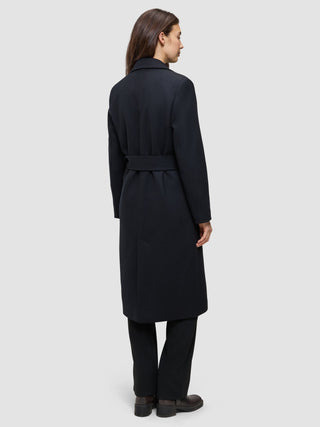 Eine Frau wird von hinten gezeigt. Sie trägt einen schwarzen Damenmantel aus Wolle in minimalistischem skandinavischem Design mit einer langen Silhouette und Gürtel.
