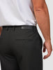 Eine Person, die eine schwarze „Essential Suit Pants Relaxed Fit“-Hose mit einer Gesäßtasche und einem Markenetikett am Bund trägt.