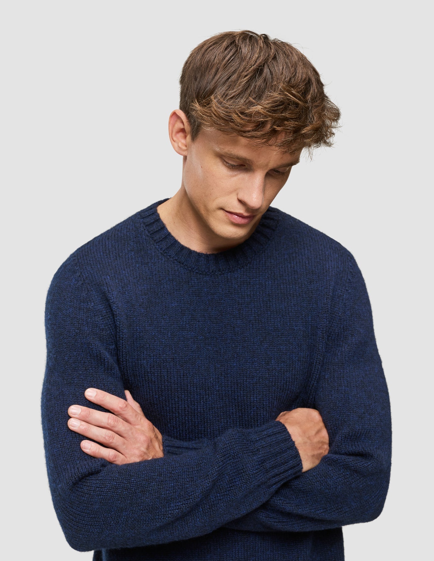 Ein Mann mit verschränkten Armen, der einen dicken, weichen Wollpullover mit Rundhalsausschnitt in dunklem Marineblau-Melange trägt.