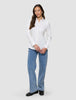 Eine Frau, die ein Damen-Oxford-Hemd White Orchid Slim mit klassischem Kragen trägt, das in eine blaue Jeans gesteckt ist, dazu schwarze Loafer.