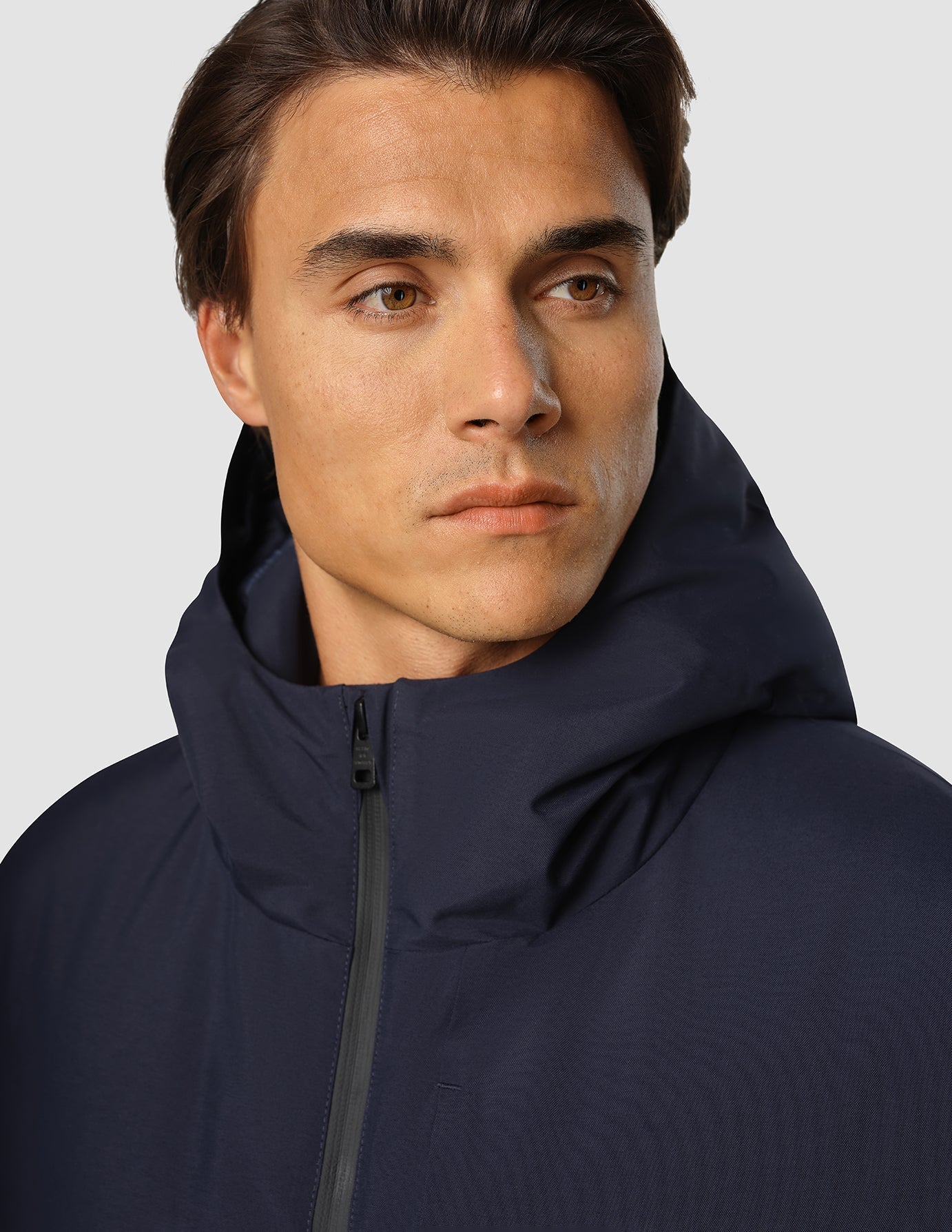 Eine Person, die eine wasserdichte Utility-Jacke in Dunkelblau trägt, die sich durch ein dunkelblaues Kapuzendesign mit Reißverschluss vorne auszeichnet.
