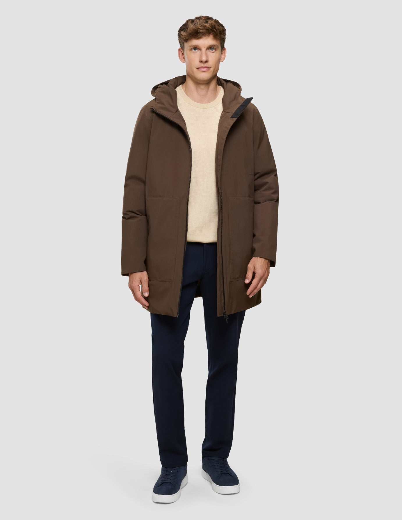 Ein Mann trägt eine winddichte Utility-Jacke in Sattelbraun über einem beigen Pullover und einer dunklen Hose.