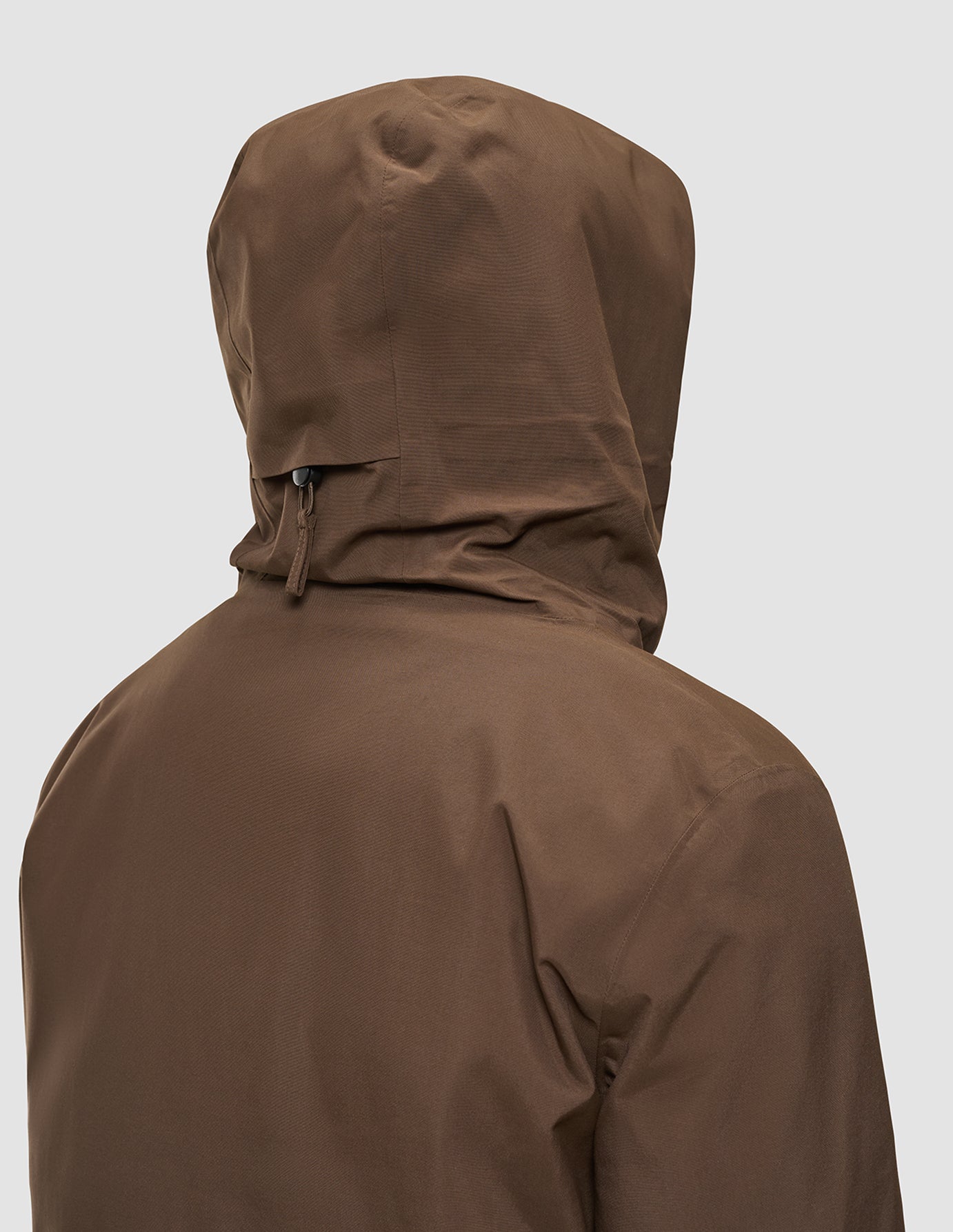 Eine Person, von hinten gesehen, die eine winddichte Utility-Jacke in Sattelbraun mit Kapuze trägt.