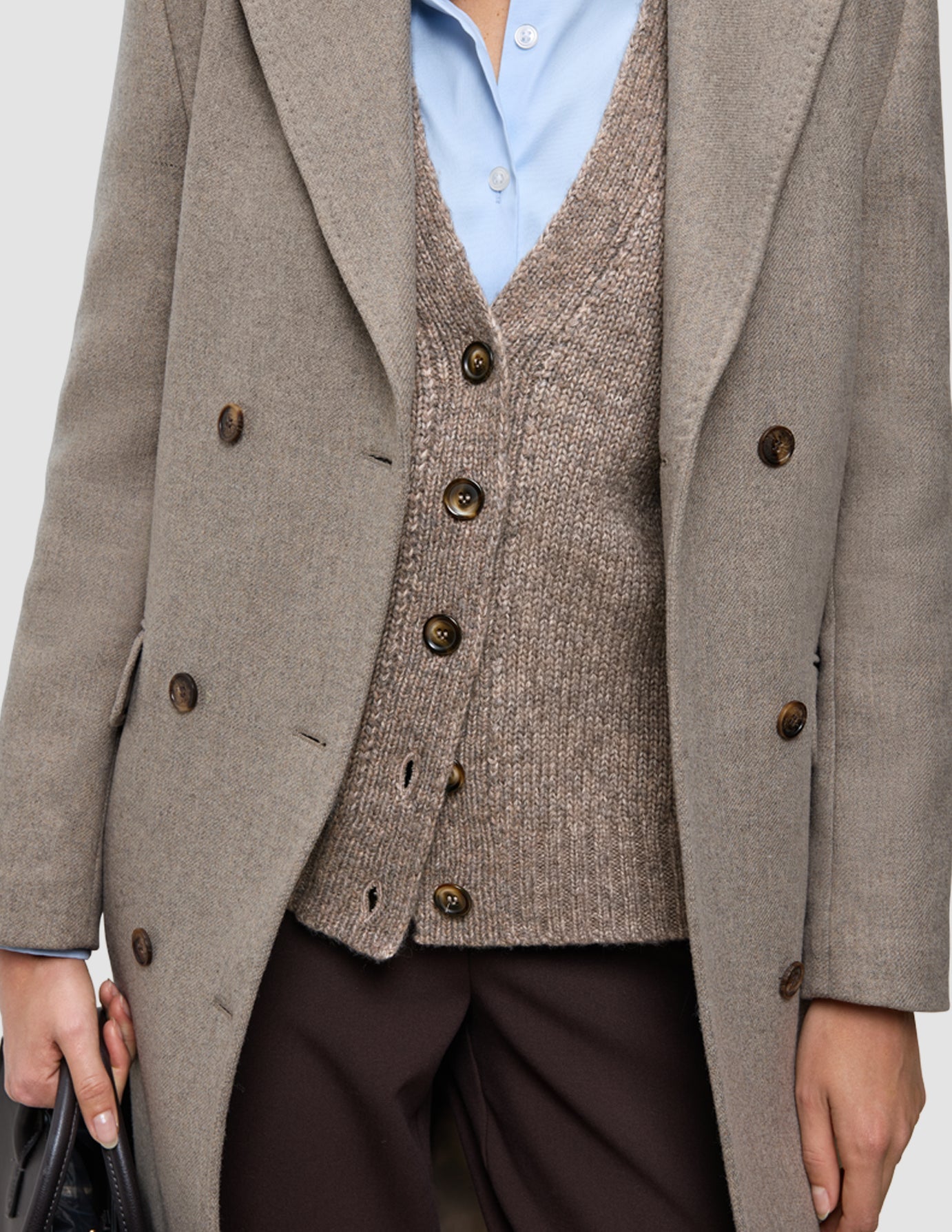 Arbeitskleidung für kaltes Wetter, bestehend aus einem hellbraunen Wollmantel, der über einer gestrickten Strickjacke mit Knöpfen getragen wird, einem hellblauen Oxford-Hemd und einer dunklen Hose.