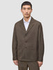 Ein Mann trägt ein Atelier Overshirt Dark Beige aus gebrochenem Twill mit Kragen, drei Knöpfen und zwei großen aufgesetzten Taschen über einem weißen Hemd mit Kragen, was ein klares, skandinavisches Design widerspiegelt.