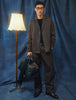 Eine Person, die ein dunkelbeiges Atelier Overshirt und eine dazu passende Hose aus gebrochenem Twill trägt, hält eine schwarze Reisetasche in der Hand.