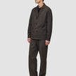 Ein Mann, der ein dunkelbraunes Overshirt von Atelier trägt, dazu eine passende Hose und darunter ein schwarzes T-Shirt.