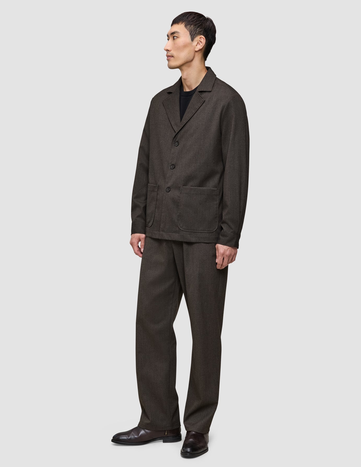 Ein Mann, der ein dunkelbraunes Overshirt von Atelier trägt, dazu eine passende Hose und darunter ein schwarzes T-Shirt.