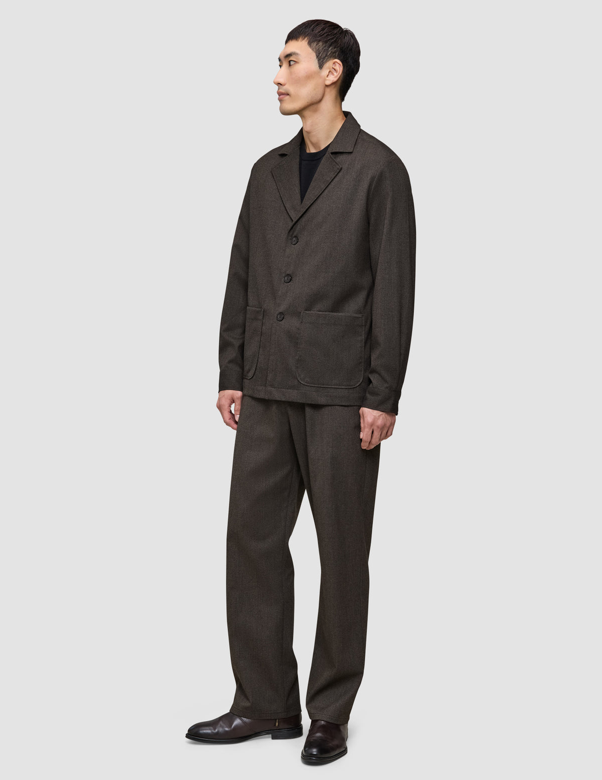 Ein Mann, der ein dunkelbraunes Overshirt von Atelier trägt, dazu eine passende Hose und darunter ein schwarzes T-Shirt.