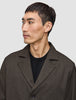 Eine Person, die ein dunkelbraunes Atelier Overshirt mit gekerbtem Kragen über einem schwarzen T-Shirt mit Rundhalsausschnitt trägt.