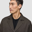 Eine Person, die ein dunkelbraunes Atelier Overshirt mit gekerbtem Kragen über einem schwarzen T-Shirt mit Rundhalsausschnitt trägt.