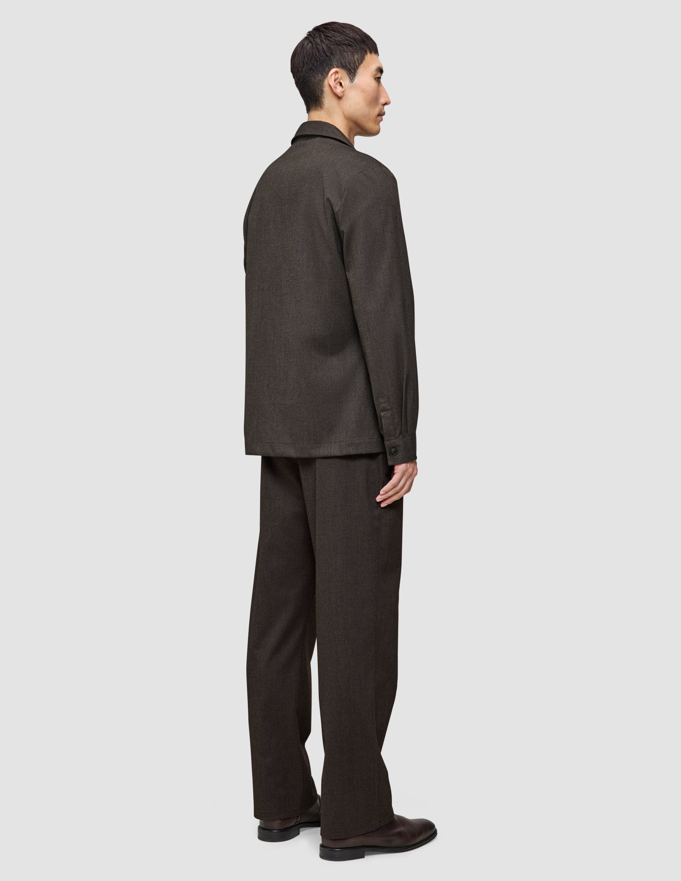 Eine Person, von der Seite gesehen, die ein dunkelbraunes Atelier Overshirt aus gebrochenem Twill und eine dazu passende Hose trägt.