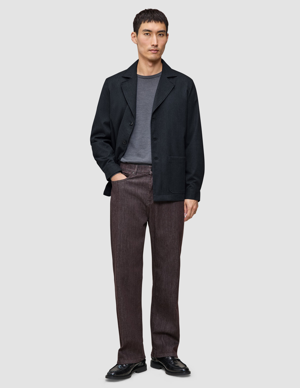 Ein Mann, der ein Atelier Overshirt Dark Navy über einem grauen T-Shirt, eine braune Atelier-Hose und schwarze Lederschuhe trägt.