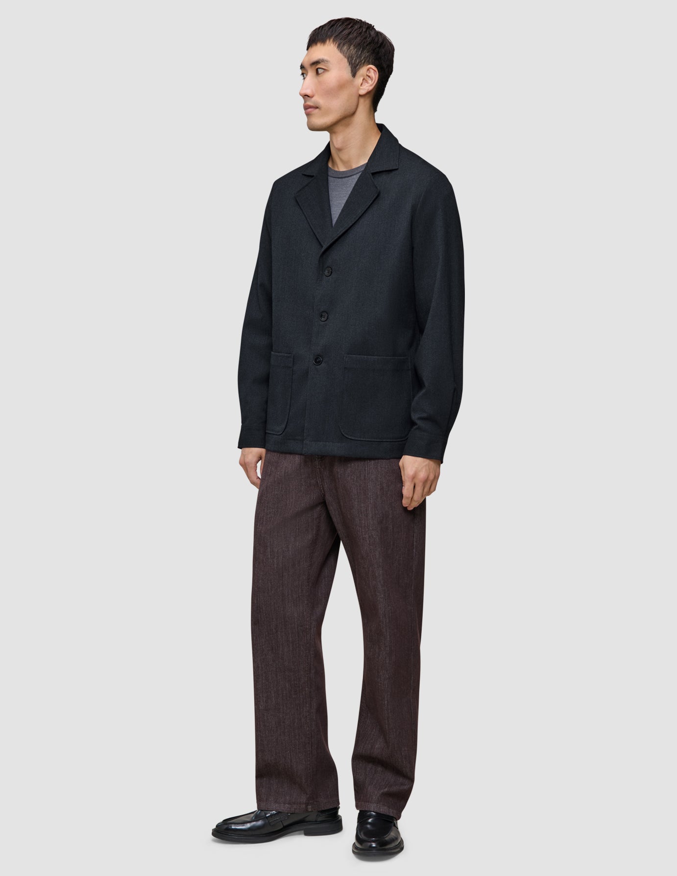 Ein Mann trägt ein dunkelblaues Atelier Overshirt über einem grauen T-Shirt, dazu eine Atelier-Hose und schwarze Loafer.