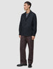 Ein Mann trägt ein dunkelblaues Atelier Overshirt über einem grauen T-Shirt, dazu eine Atelier-Hose und schwarze Loafer.