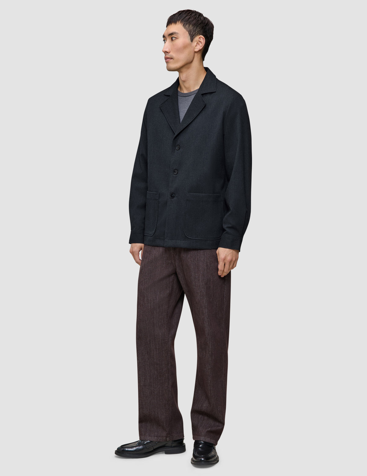 Ein Mann trägt ein dunkelblaues Atelier Overshirt über einem grauen T-Shirt, dazu eine Atelier-Hose und schwarze Loafer.