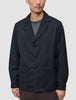 Atelier-Overshirt in Dunkelblau mit gekerbtem Kragen, drei Knöpfen und zwei aufgesetzten Vordertaschen, getragen über einem grauen Hemd.