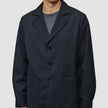 Atelier-Overshirt in Dunkelblau mit gekerbtem Kragen, drei Knöpfen und zwei aufgesetzten Vordertaschen, getragen über einem grauen Hemd.