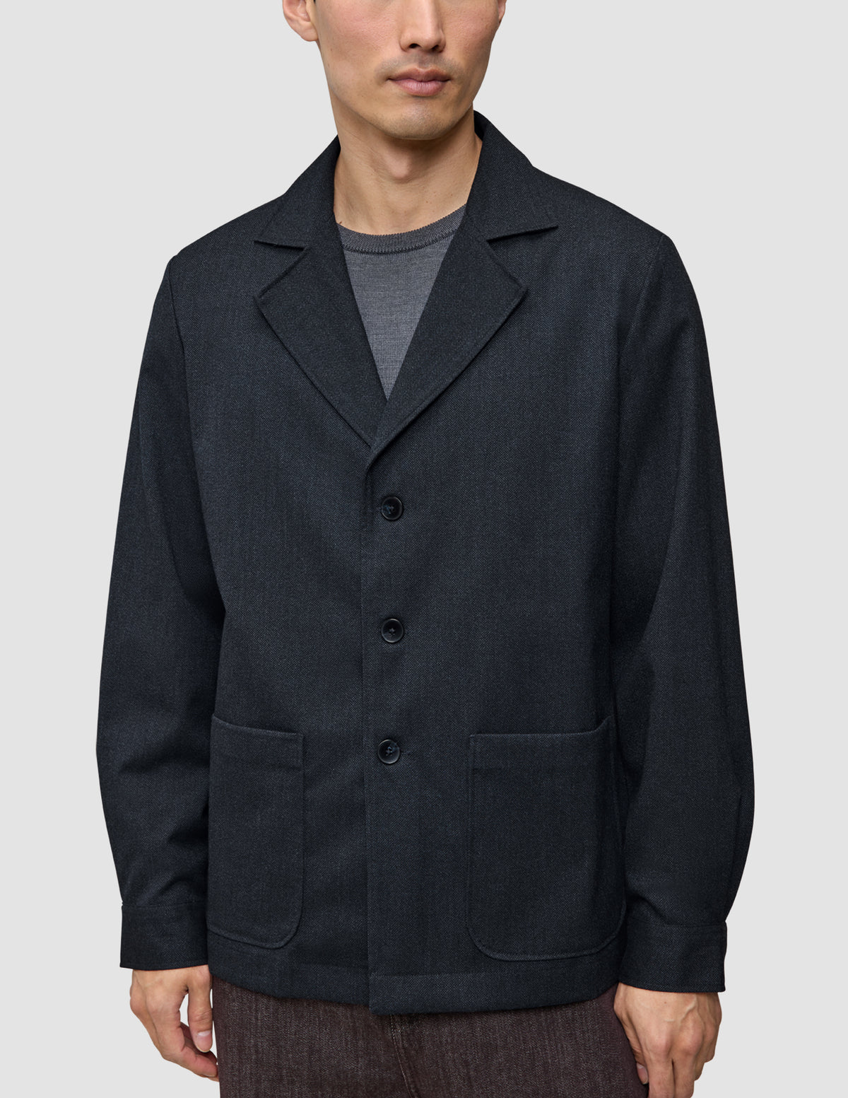 Atelier-Overshirt in Dunkelblau mit gekerbtem Kragen, drei Knöpfen und zwei aufgesetzten Vordertaschen, getragen über einem grauen Hemd.
