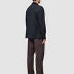 Eine Person, von hinten gesehen, die ein Atelier Overshirt Dark Navy, eine Atelier-Hose und schwarze Schuhe trägt.