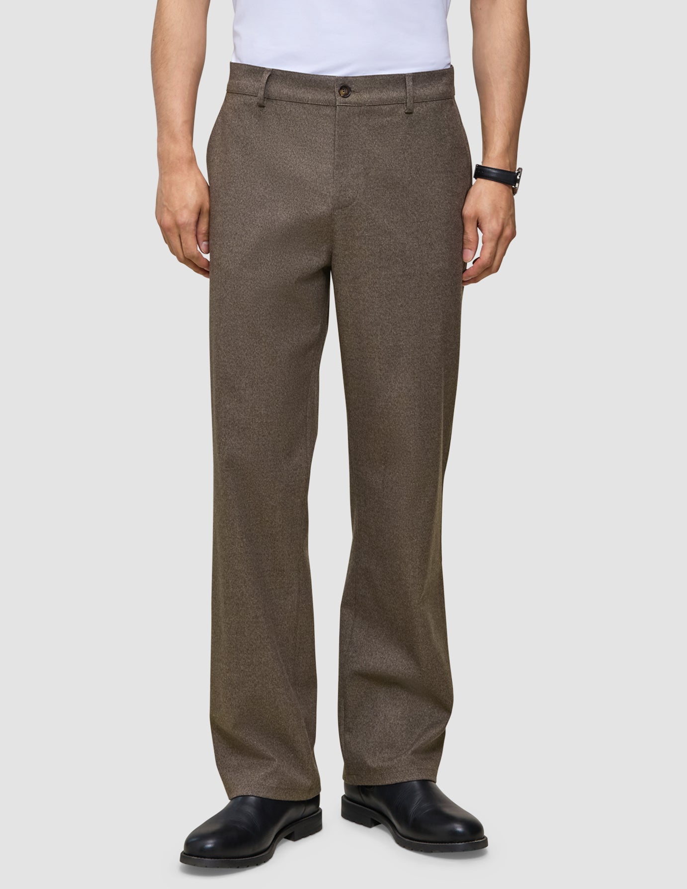 Eine Person trägt die Atelier Pants Relaxed in Dunkelbeige aus schwerem, gebrochenem Twill sowie schwarze Lederschuhe.
