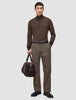 Ein Mann in einem braunen Pullover mit Viertelreißverschluss und einer Atelier Pants Relaxed in Dunkelbeige, der eine dunkelbraune Reisetasche im skandinavischen Design in der Hand hält.