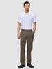 Ein Mann trägt ein weißes T-Shirt, schwarze Schuhe und eine Atelier Pants Relaxed Dark Beige aus schwerem Broken-Twill.