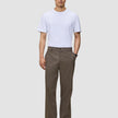 Ein Mann trägt ein weißes T-Shirt, schwarze Schuhe und eine Atelier Pants Relaxed Dark Beige aus schwerem Broken-Twill.
