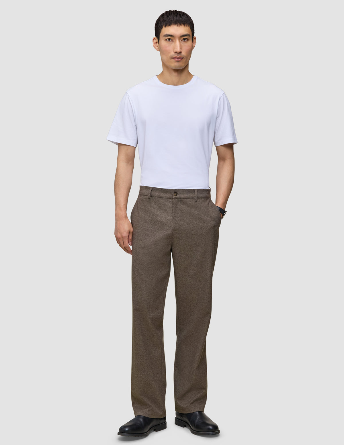 Ein Mann trägt ein weißes T-Shirt, schwarze Schuhe und eine Atelier Pants Relaxed Dark Beige aus schwerem Broken-Twill.