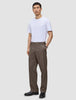 Ein Mann, der ein weißes T-Shirt und eine Atelier Pants Relaxed Dark Beige aus schwerem Broken-Twill trägt, dazu schwarze Lederschuhe.