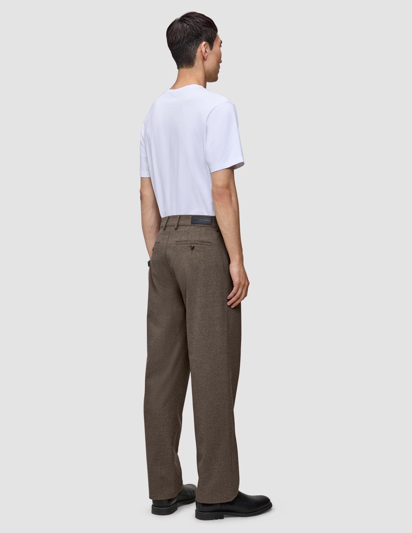 Ein Mann, von hinten gesehen, der ein weißes T-Shirt und eine Atelier Pants Relaxed in Dunkelbeige aus schwerem Broken-Twill trägt.