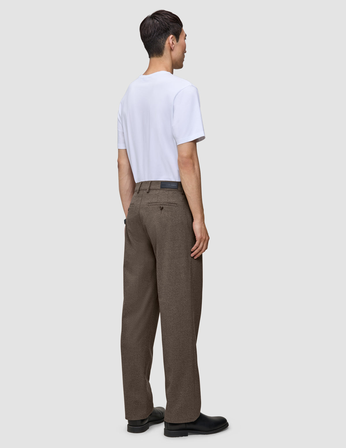 Ein Mann, von hinten gesehen, der ein weißes T-Shirt und eine Atelier Pants Relaxed in Dunkelbeige aus schwerem Broken-Twill trägt.