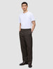 Ein Mann, der ein weißes T-Shirt und eine Atelier Pants Relaxed in Dunkelbraun aus schwerem Broken-Twill trägt und die Hände in den Taschen hat.