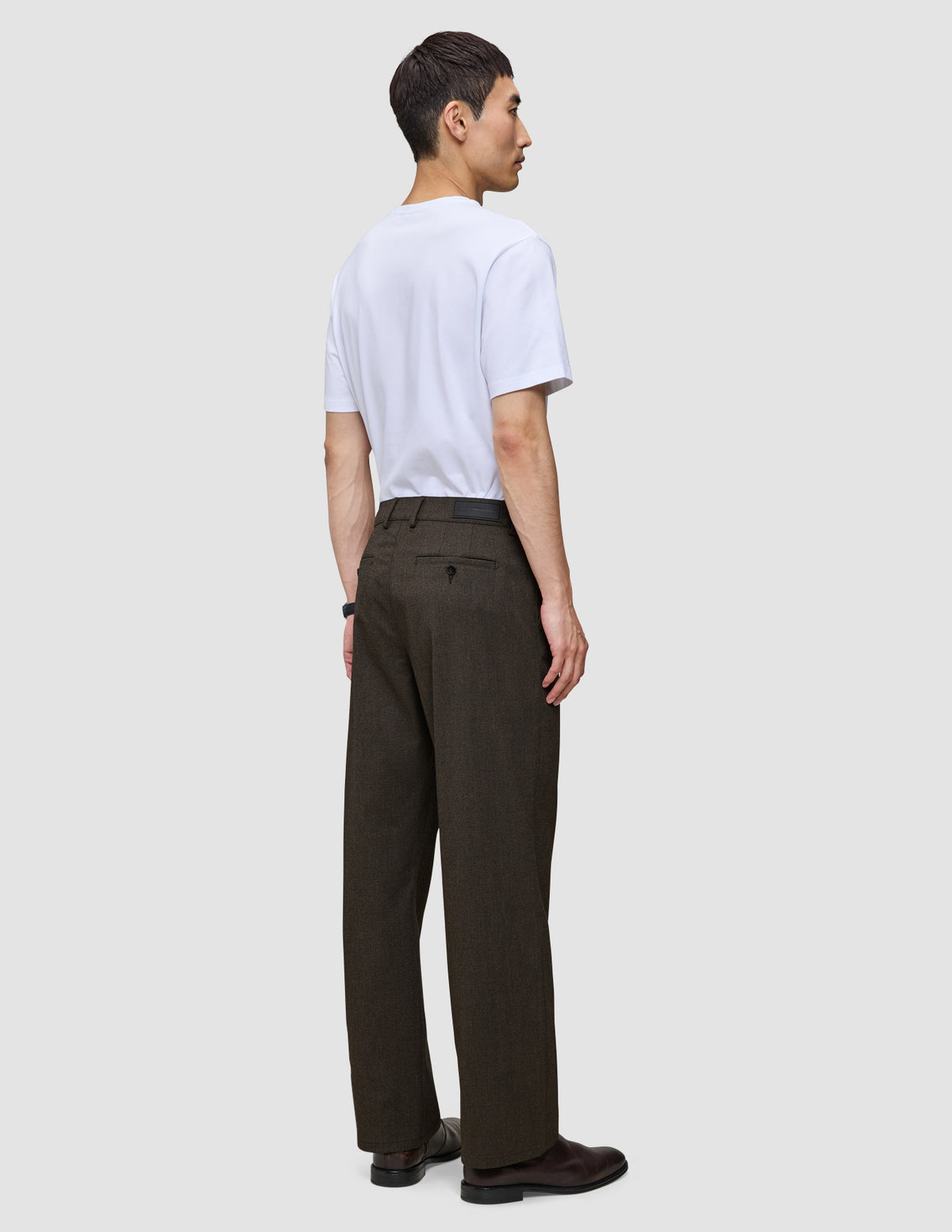 Eine Person, von hinten gesehen, die ein weißes T-Shirt und eine Atelier Pants Relaxed in Dunkelbraun aus schwerem, gebrochenem Twill trägt.